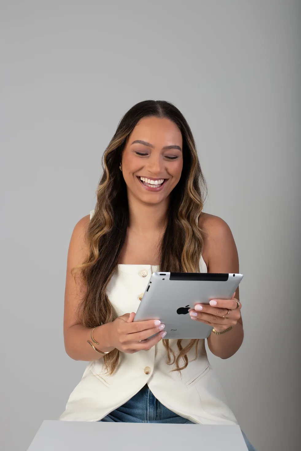 Mulher rindo enquanto olha para a tela de um tablet que segura com as duas mãos.