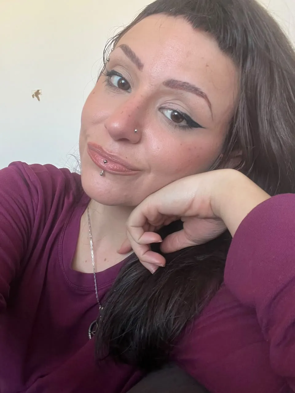 Giovanna, de cabelos longos escuros e blusa vinho, apoiando o rosto na mão.