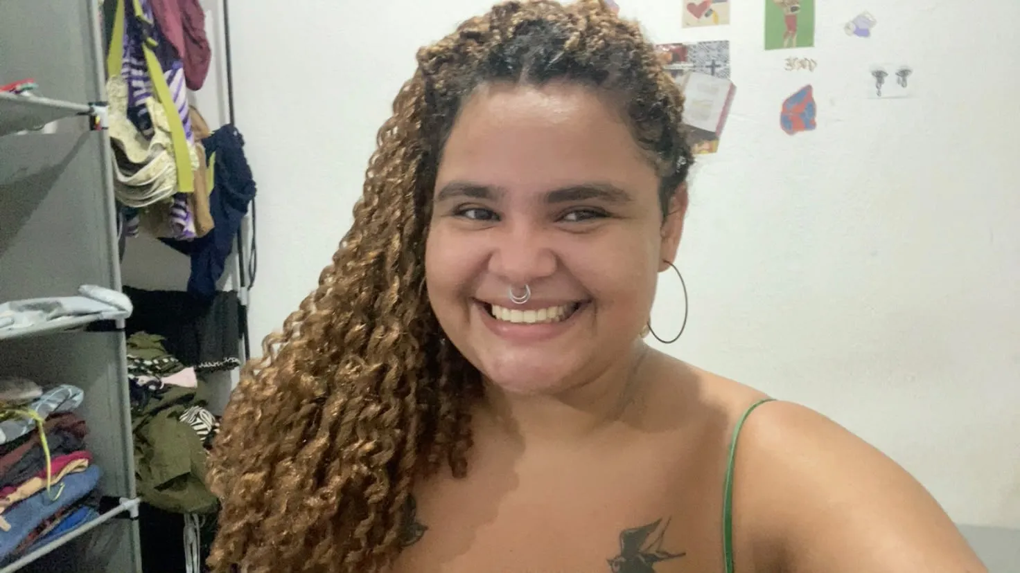 Karen, de cabelos longos cacheados e argola nas orelhas, sorrindo em uma selfie.
