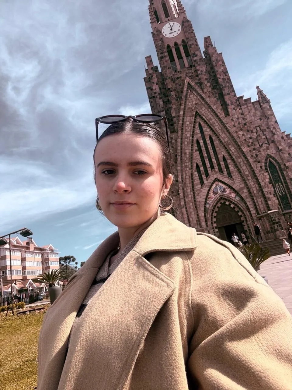 Luiza, de casaco bege e óculos de sol na cabeça, diante da Catedral de Pedra de Canela.
